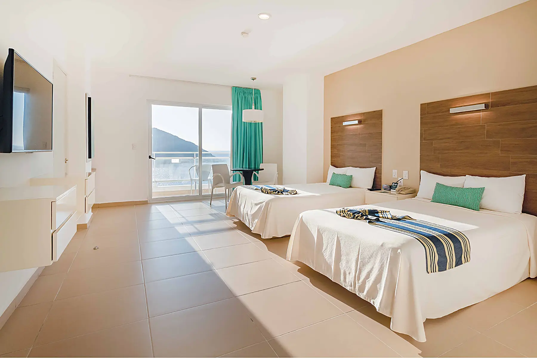 Habitación junior suite vista al mar con dos camas matrimoniales, televisión, mesa con dos sillas, mobiliario y luminaria de Hotel Pacific Palace Mazatlán